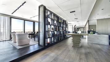 A modern hotel lobby with a large bookshelf, a reception desk, and a seating area with sofas.