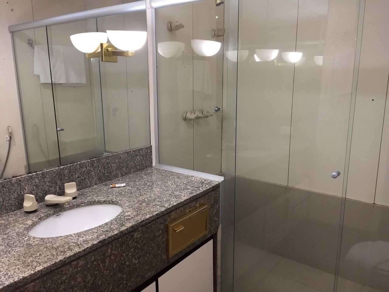 Een badkamer met een granieten aanrecht, een witte wastafel, een gouden kraan en een douchecabine van glas.