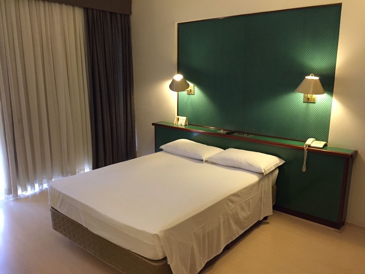Une chambre d’hôtel avec un grand lit, deux lampes de chevet, un téléphone et une tête de lit verte.