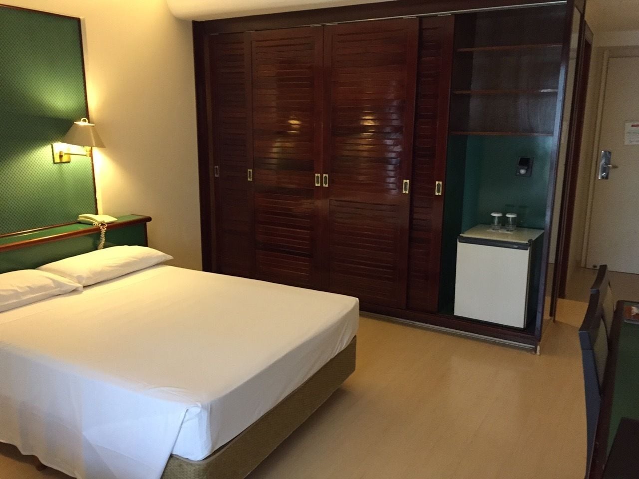 A hotel room with a bed, a desk, a wardrobe, and a minibar.