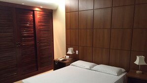 Un dormitorio con una cama, dos mesitas de noche, un armario y un panel en la pared.