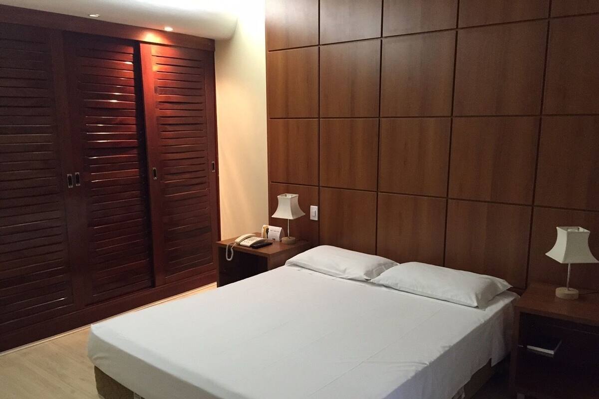 Un dormitorio con una cama, dos mesitas de noche, un armario y un panel en la pared.