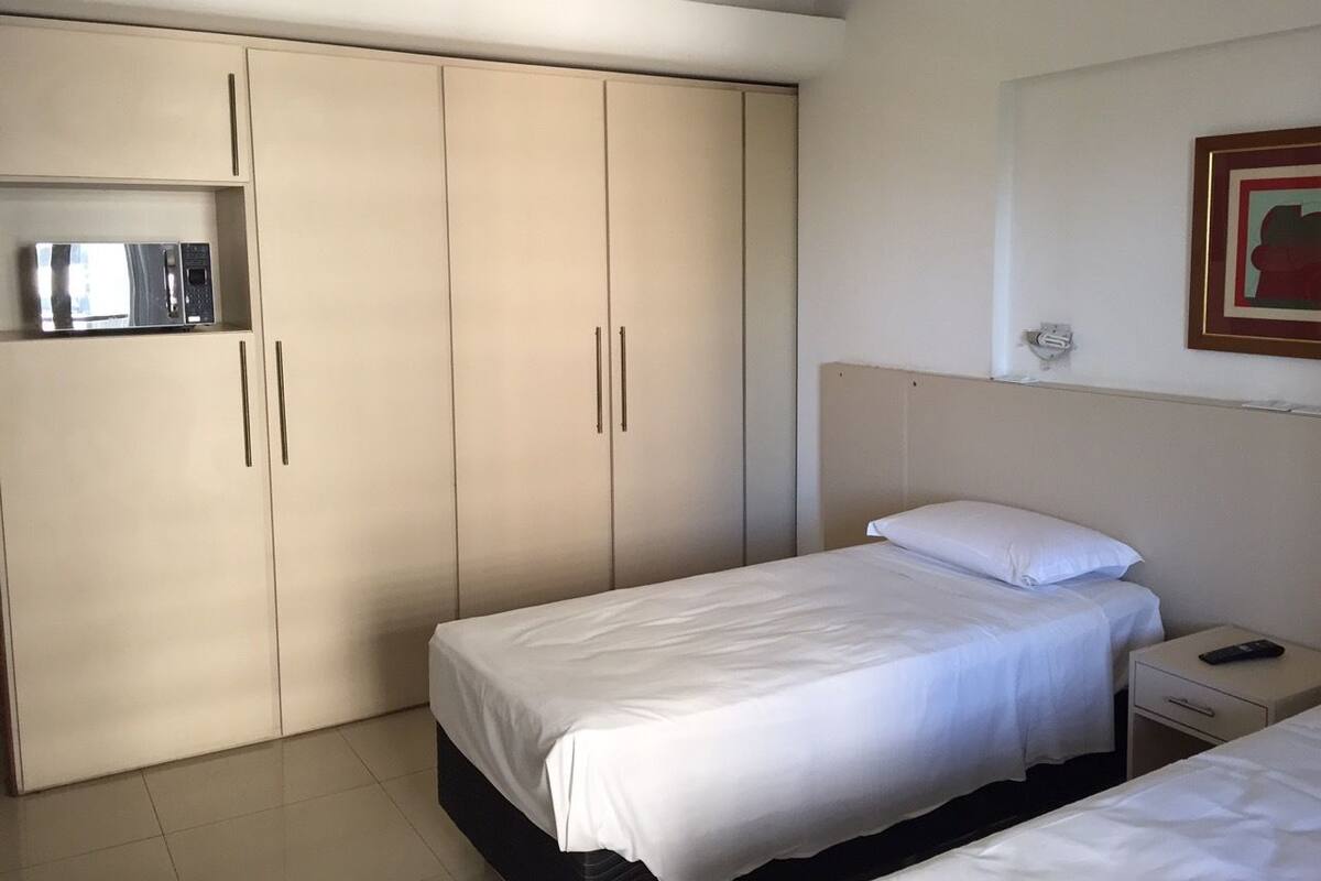 Una habitación de hotel con una cama, una mesita de noche, un microondas y un armario.