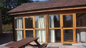 Un bâtiment en bois doté de grandes portes vitrées et d’une table de pique-nique devant.