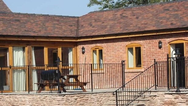 Un bâtiment en briques doté d’un patio couvert, d’un barbecue et d’un mur en pierre.