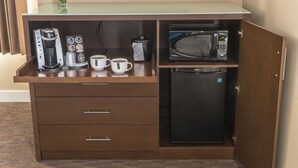 Et kompakt hotelværelse med tekøkken, inklusive kaffemaskine, mikroovn og et lille køleskab.