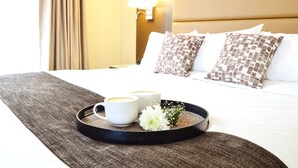 En pænt redt hotelseng med en bakke med to hvide kopper og en lille hvid blomst.