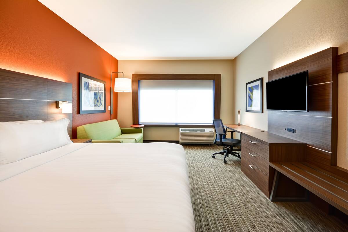 Ein Hotelzimmer mit einem großen Bett, einem Schreibtisch mit Stuhl, einem Flachbildfernseher und einem Fenster mit Jalousien.