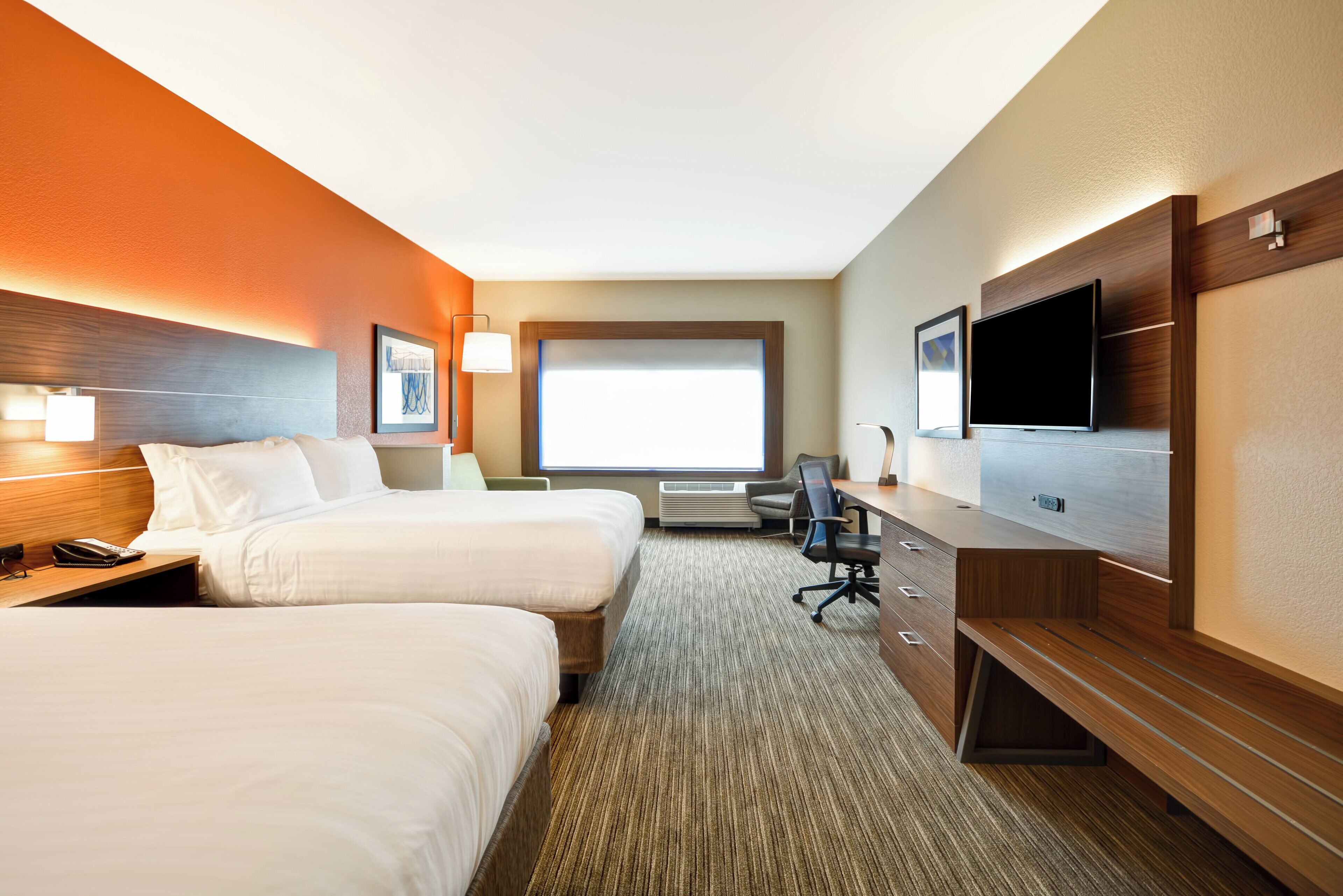 A hotel room with two beds, a desk, a chair, a TV, and a window.