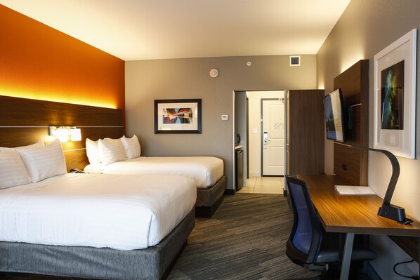 A hotel room with a large bed, a desk with a chair, a TV, and a framed picture on the wall.