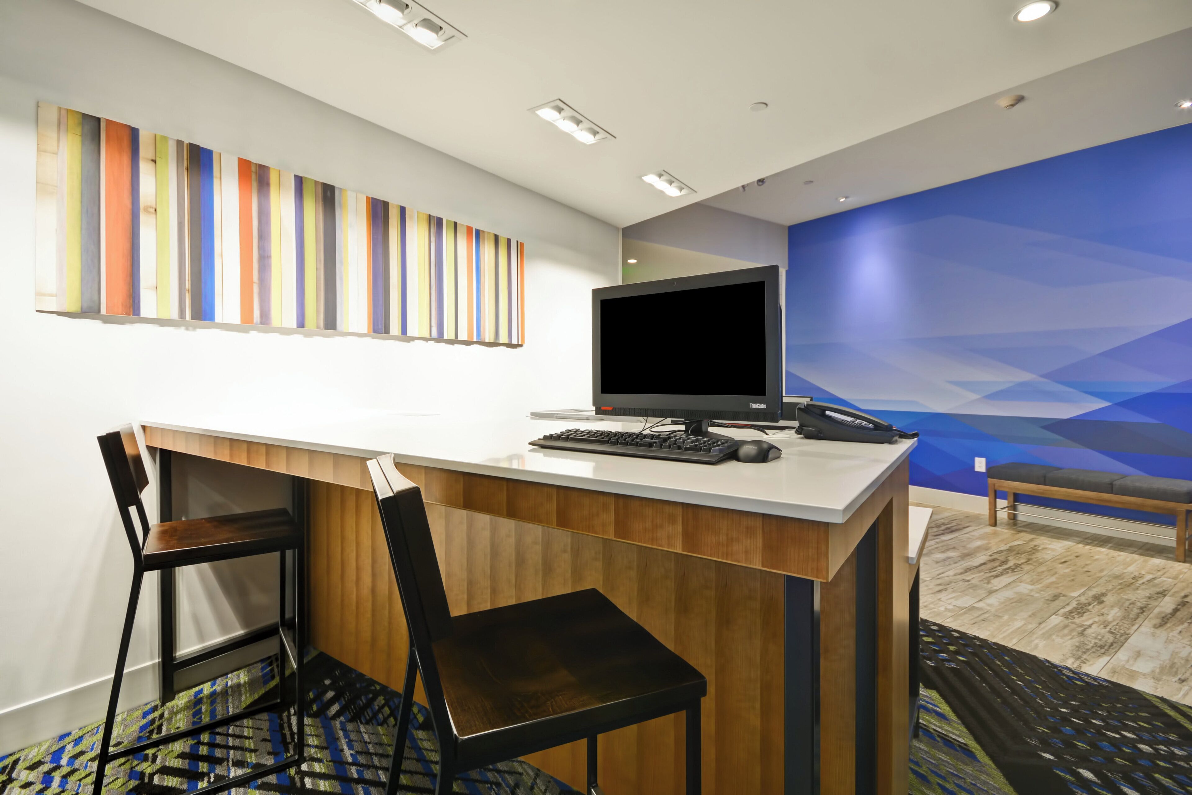 A hotel reception desk with a computer, a telephone, and a bench.