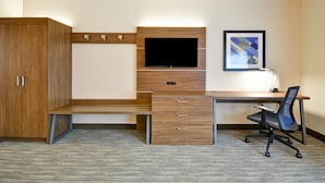 Habitación de hotel con un escritorio de madera, televisor de pantalla plana, una silla y un armario.