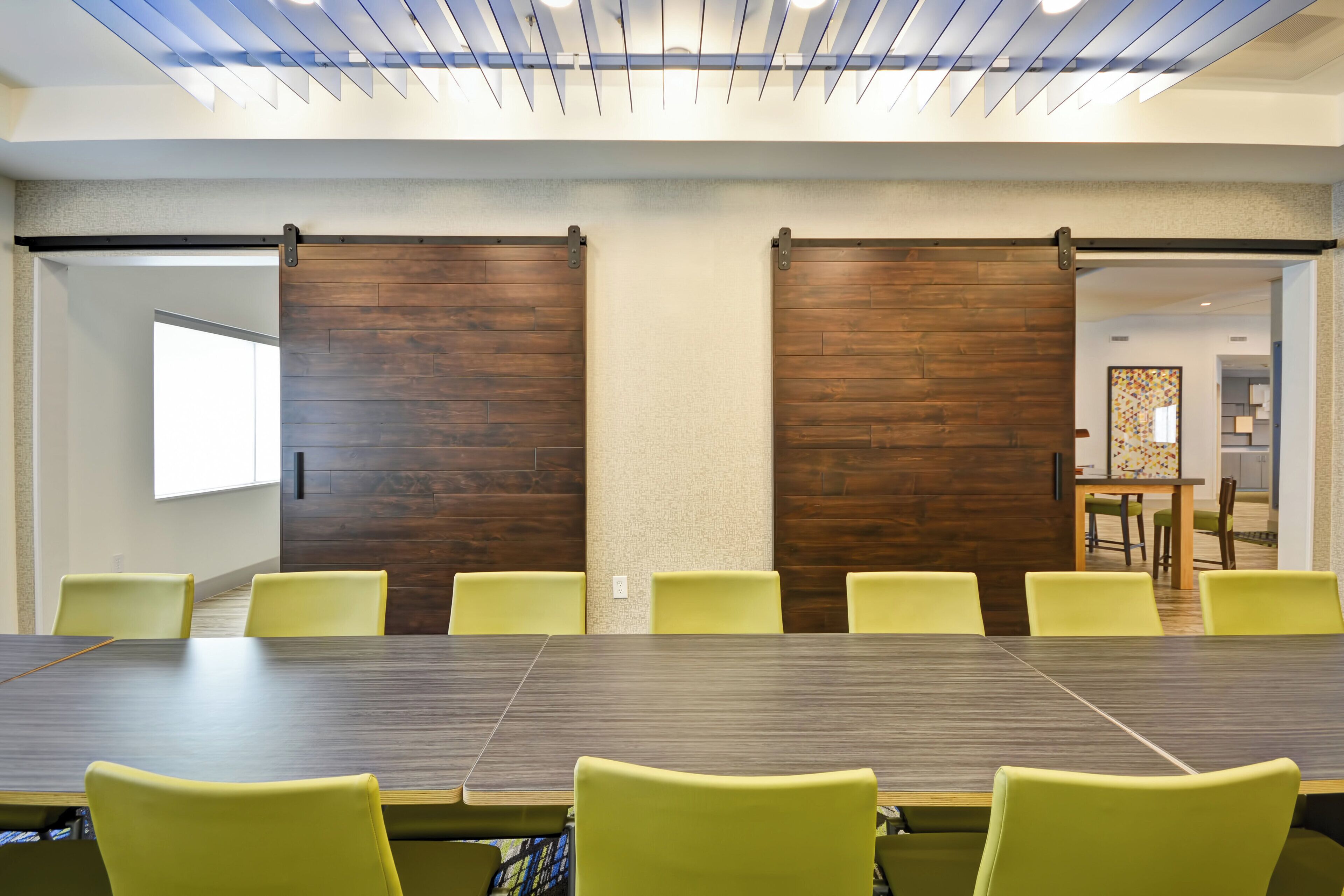 A conference room with a long table and yellow chairs, wooden panel walls, and a ceiling with a slatted design.