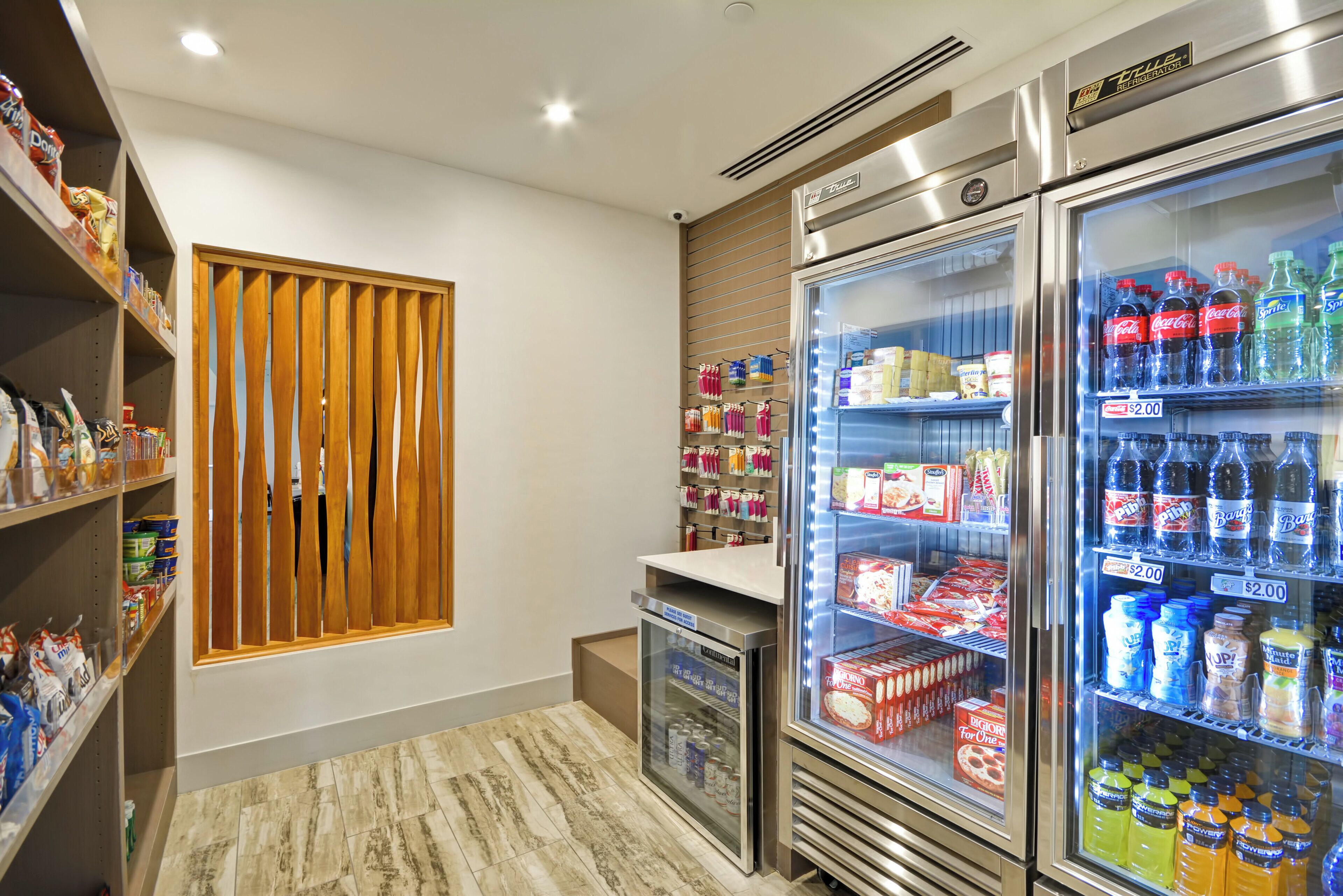 Una habitación de hotel con minibar, un refrigerador lleno de bebidas y un bar de aperitivos con diversos alimentos.