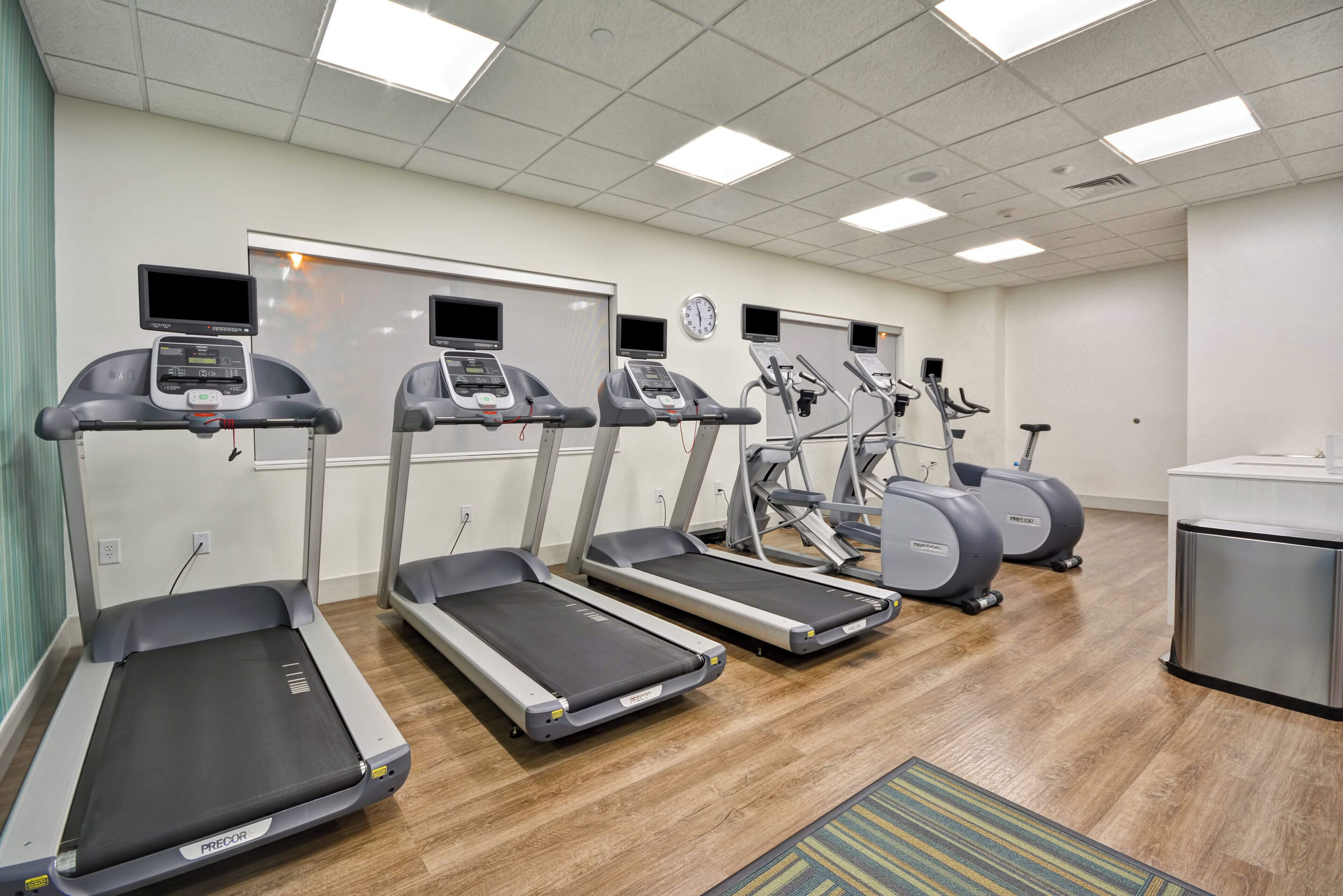 A fitness room with treadmills, elliptical machines, and a wall clock.