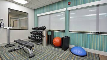 A gym with exercise equipment, a bench, a wall-mounted mirror, and a window with blinds.