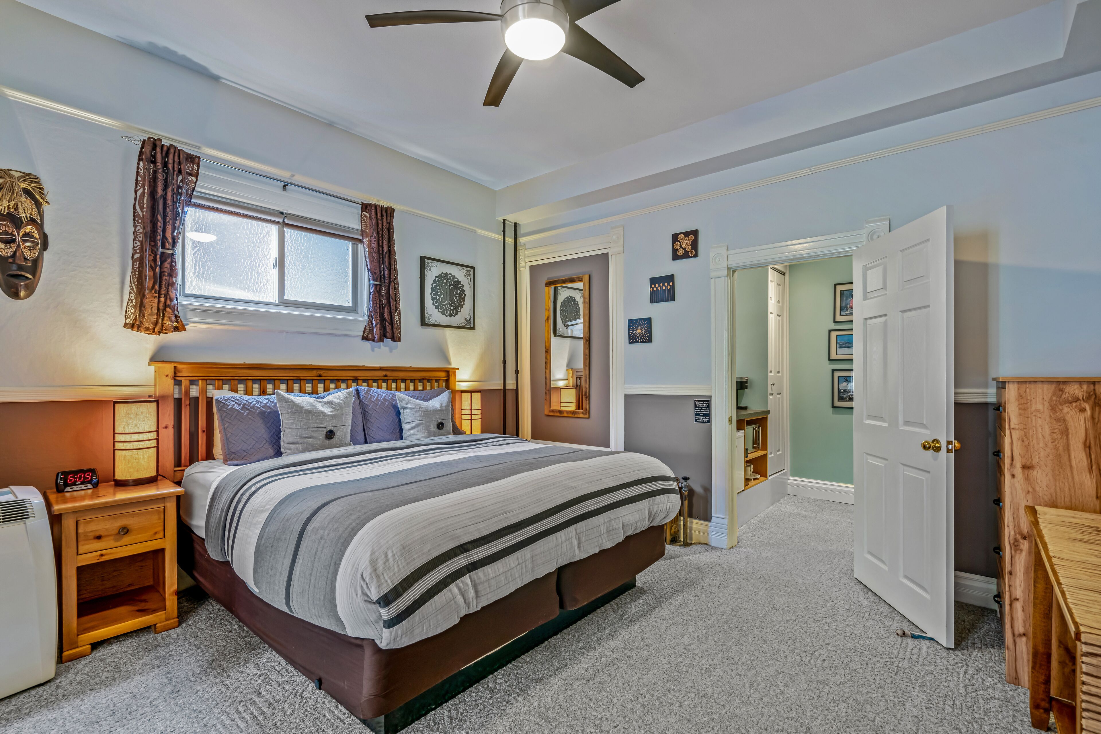 Une chambre à coucher avec un grand lit, un ventilateur de plafond, une table de chevet avec une lampe et une fenêtre avec des rideaux.