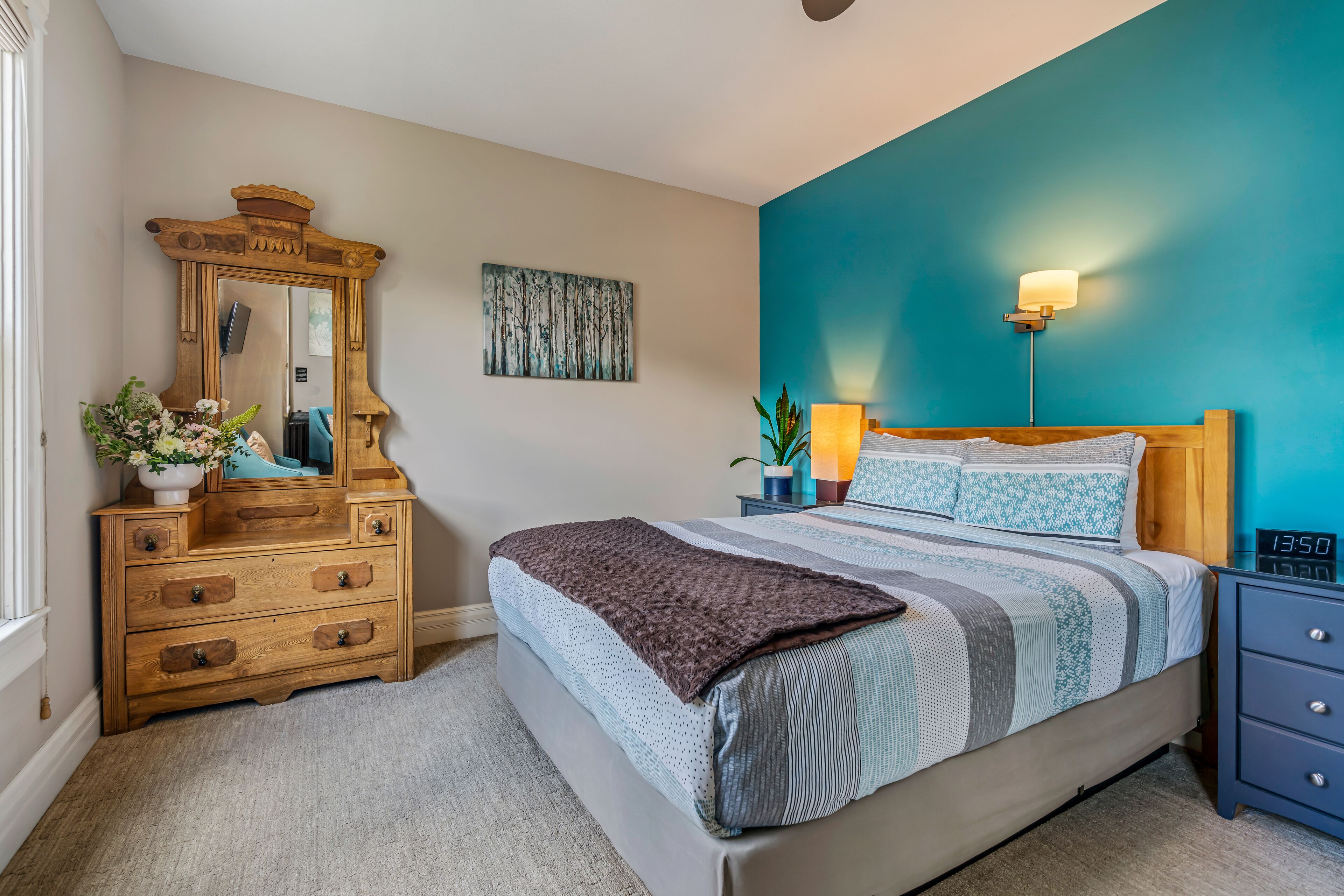 A bedroom with a bed, a dresser, a mirror, a wall clock, and a painting.