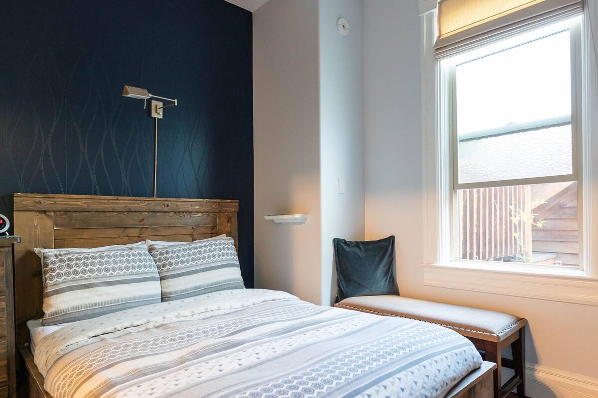 A bedroom with a bed, a desk, a chair, a ceiling fan, and a window with blinds.