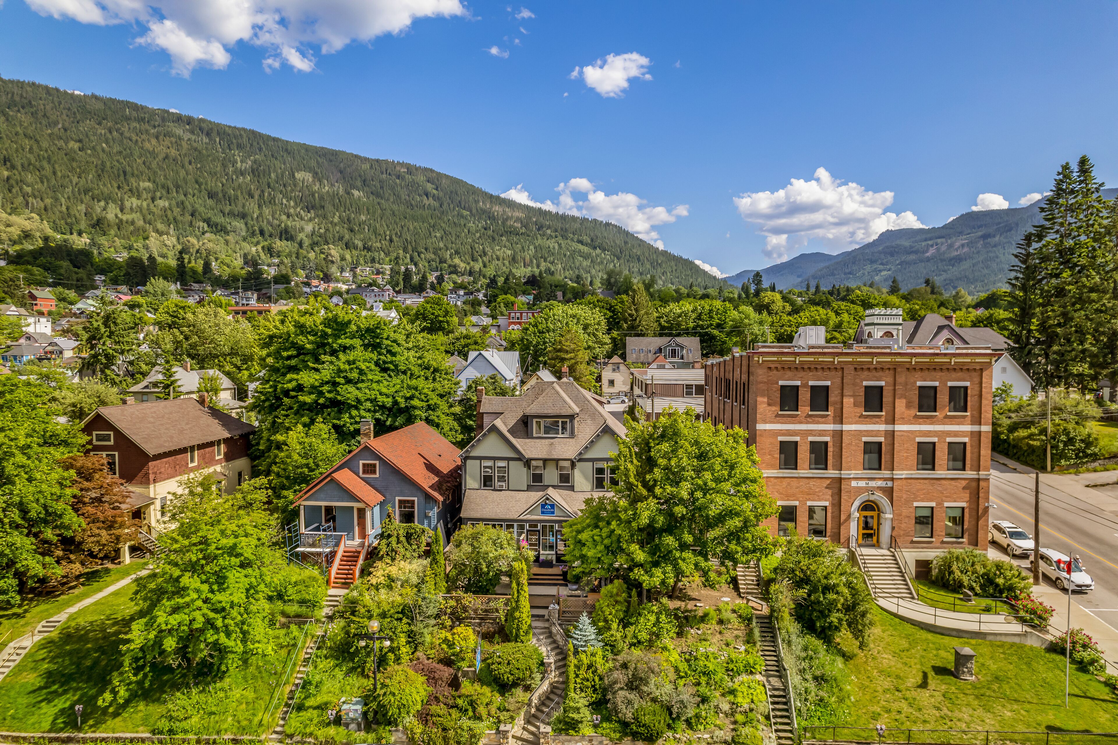 Una cittadina con un edificio in mattoni rossi ben visibile, circondata da vegetazione rigogliosa e uno sfondo montuoso.