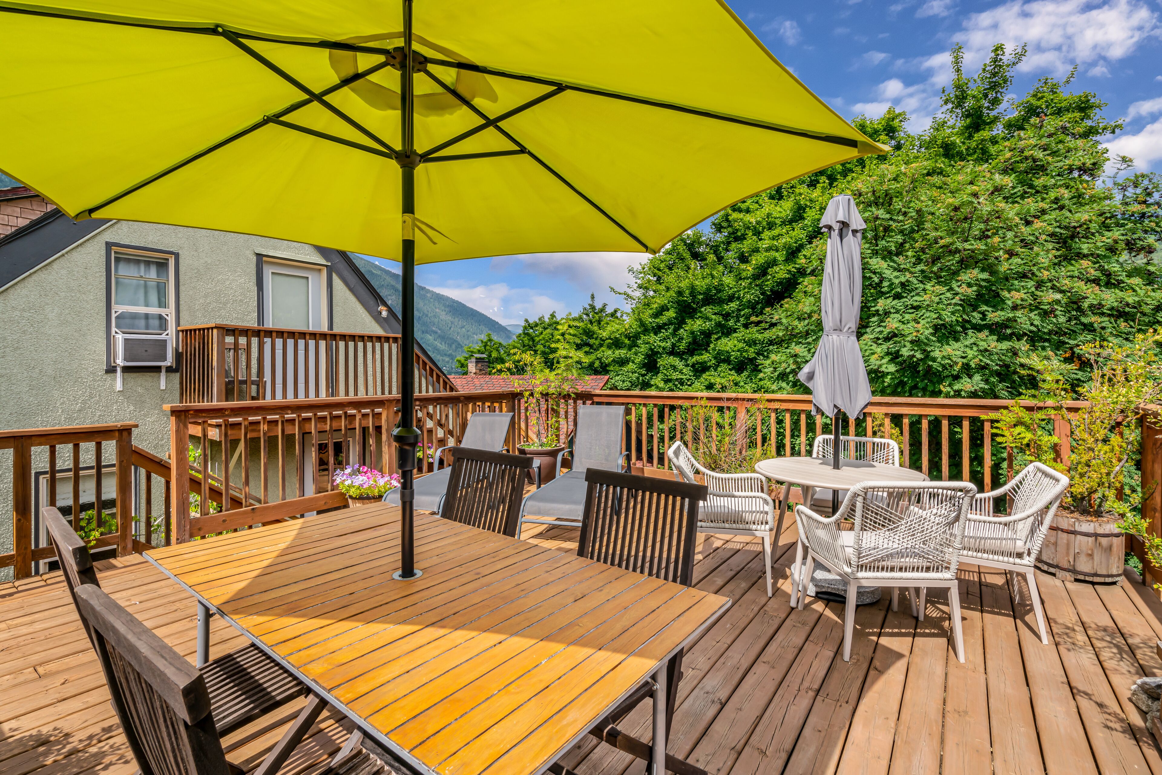 Une terrasse extérieure avec une table et des chaises en bois, un parasol jaune et un parasol blanc.