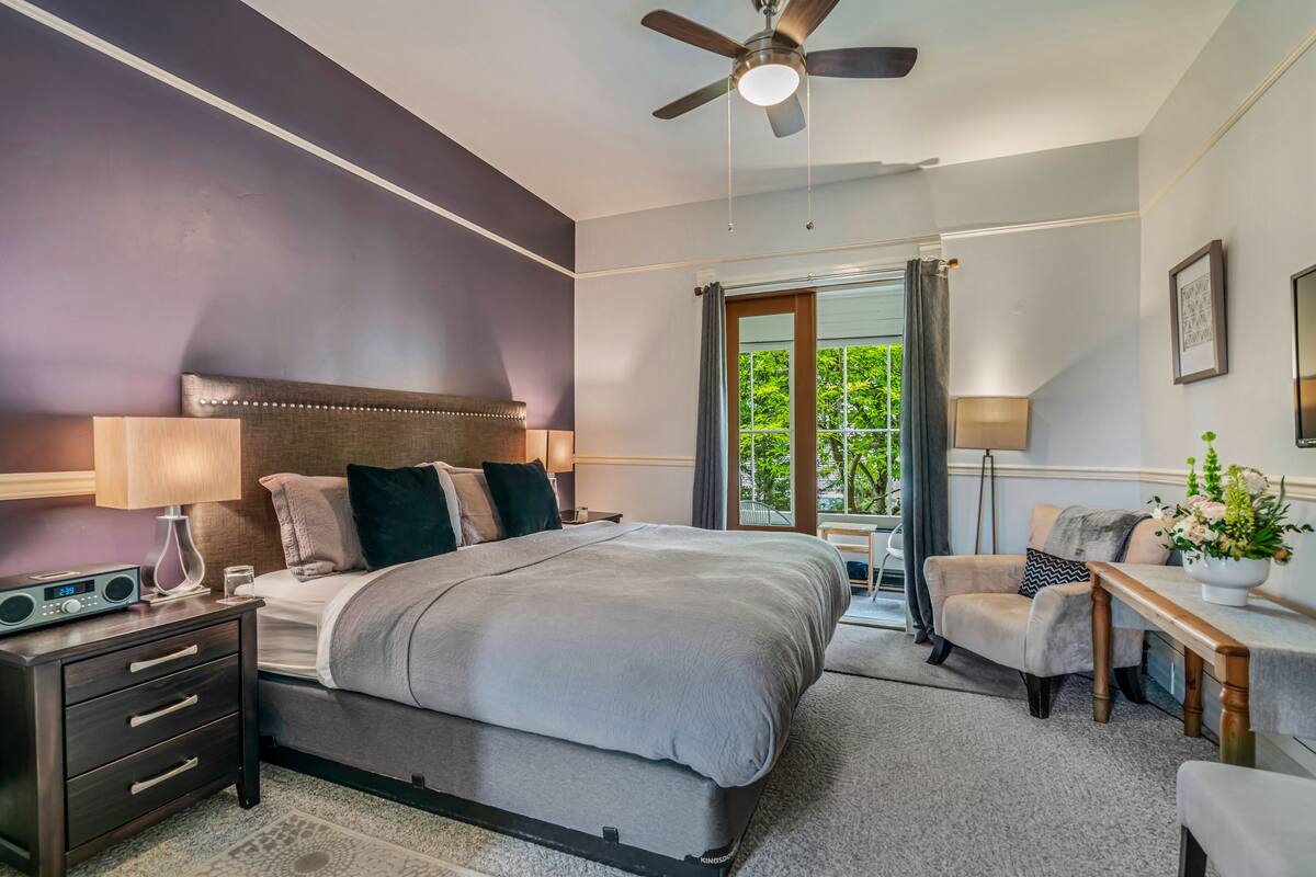 A modern bedroom with a large bed, a nightstand with a radio, a chair, and a desk with a lamp.