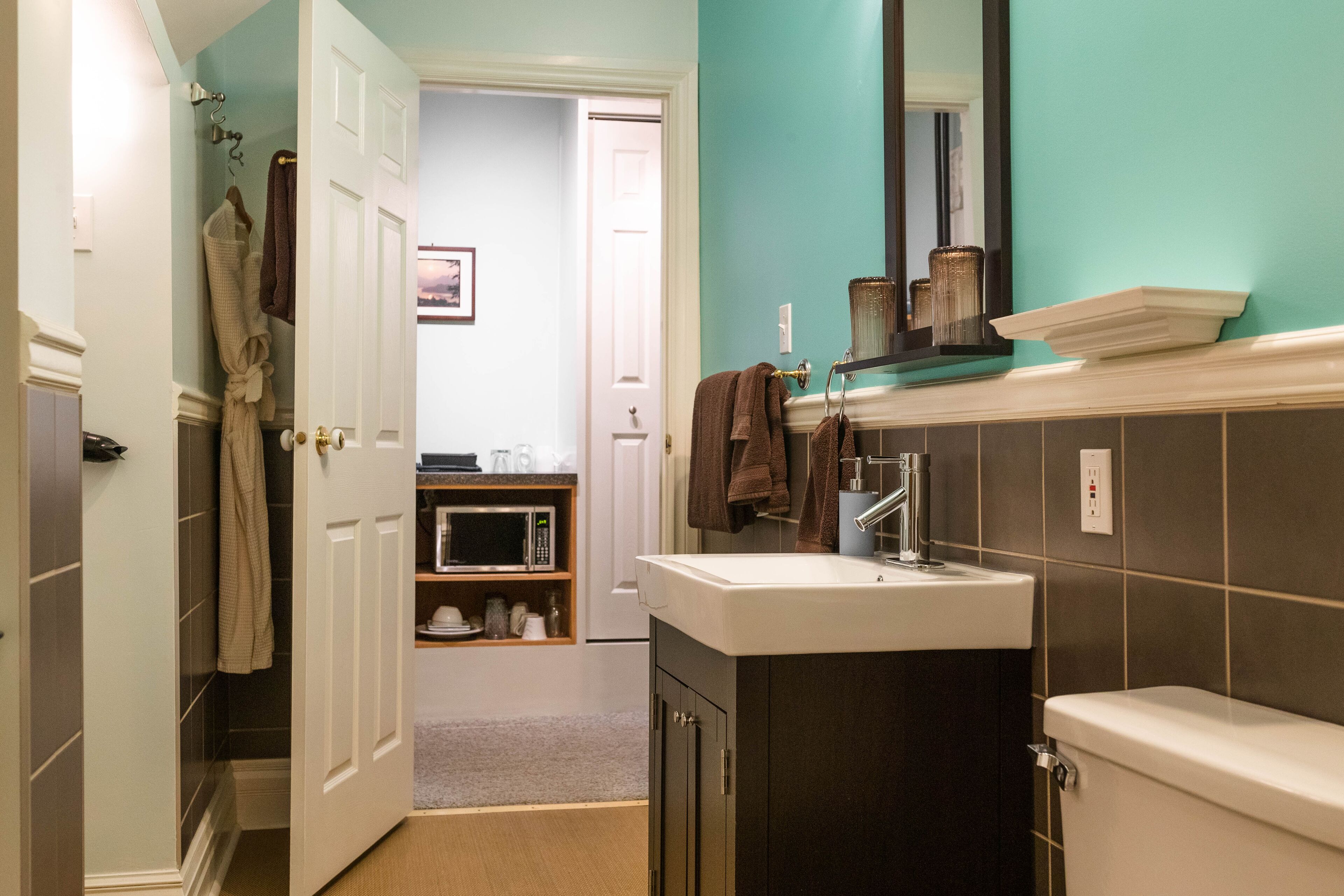 Un baño con lavamanos blanco, muebles oscuros y paredes color turquesa.