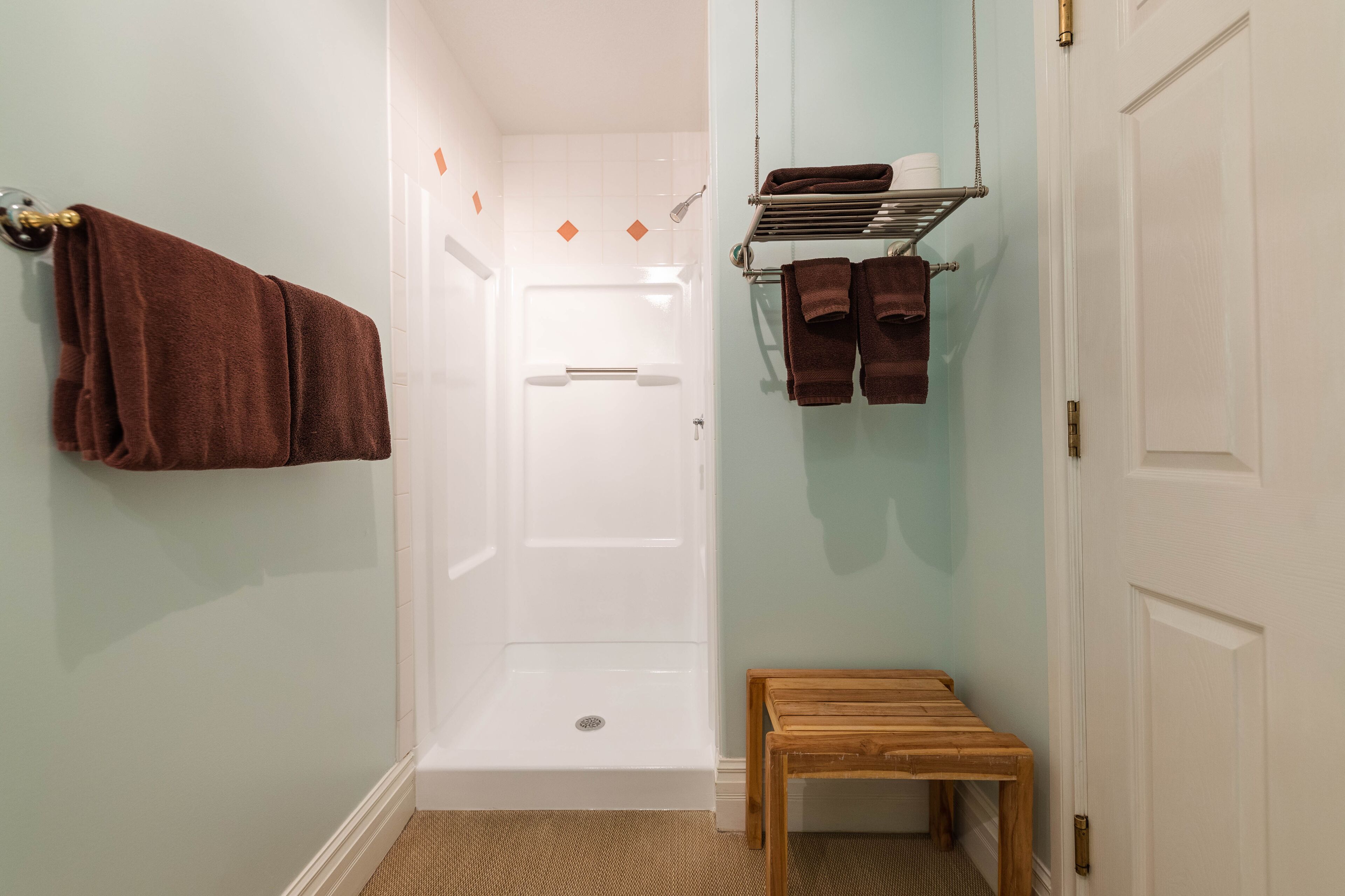 A bathroom with a shower, a towel rack with towels, and a small wooden bench.
