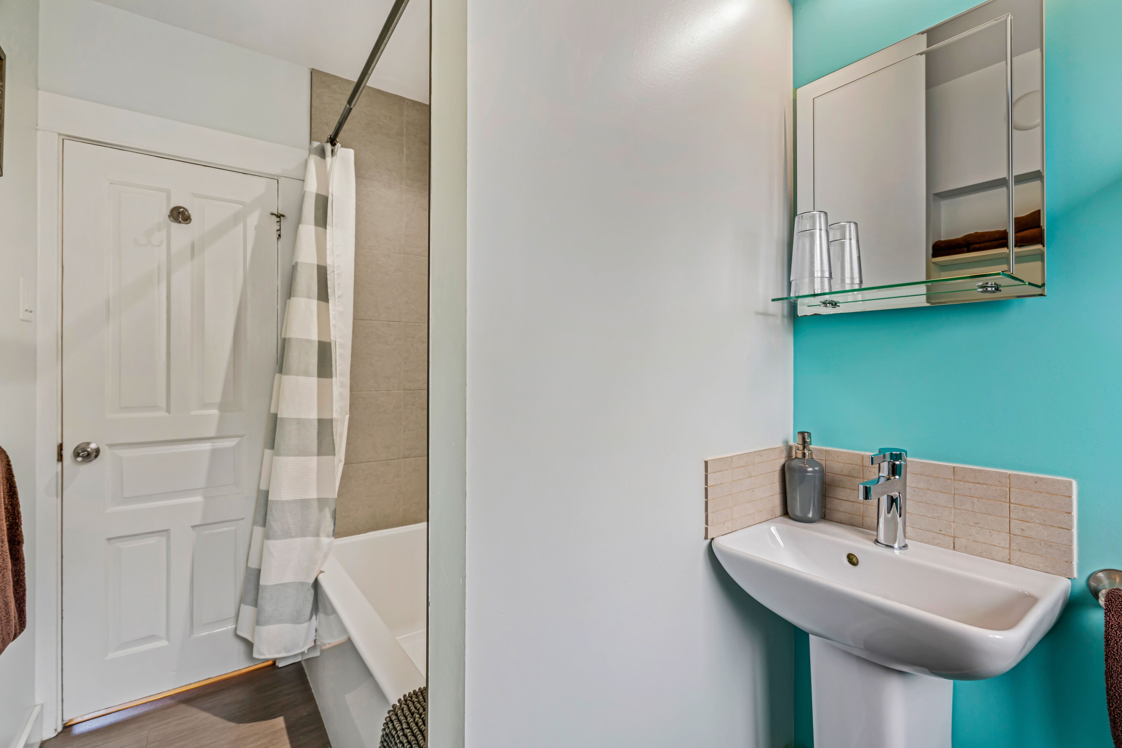 A bathroom with a white door, a striped shower curtain, a sink with a mirror above it, and a teal wall.