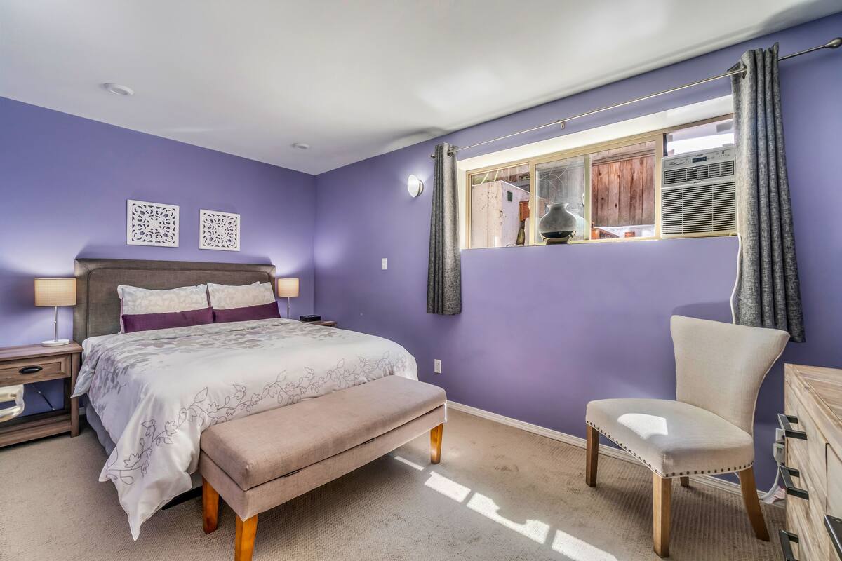 A bedroom with a bed, bedside table, chair, and a window with curtains.