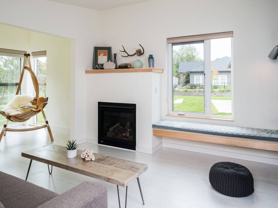 A modern living room with a fireplace, a bench by the window, and a hanging chair.