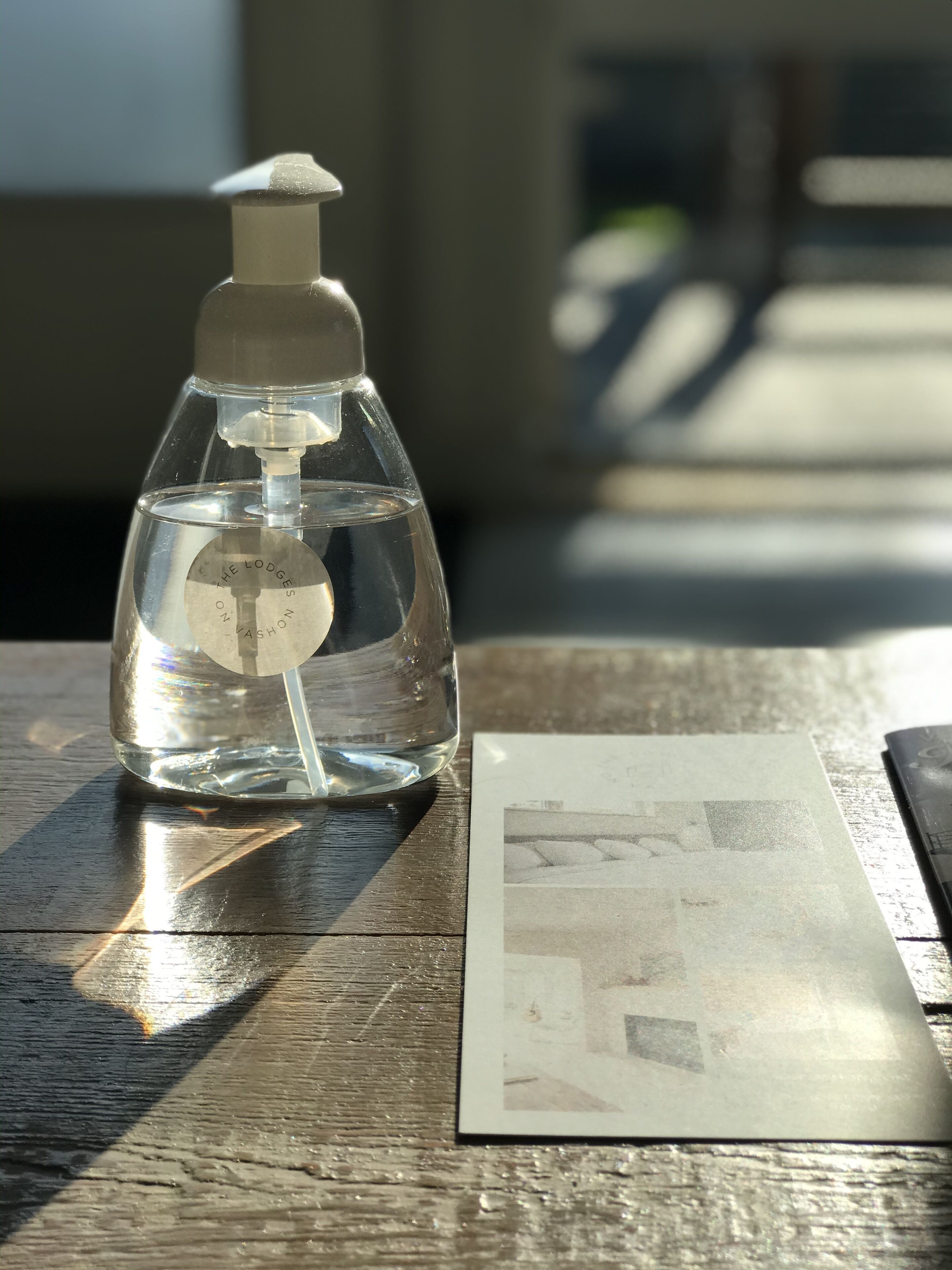 A clear glass bottle with a pump dispenser on a wooden table, next to a printed photograph.