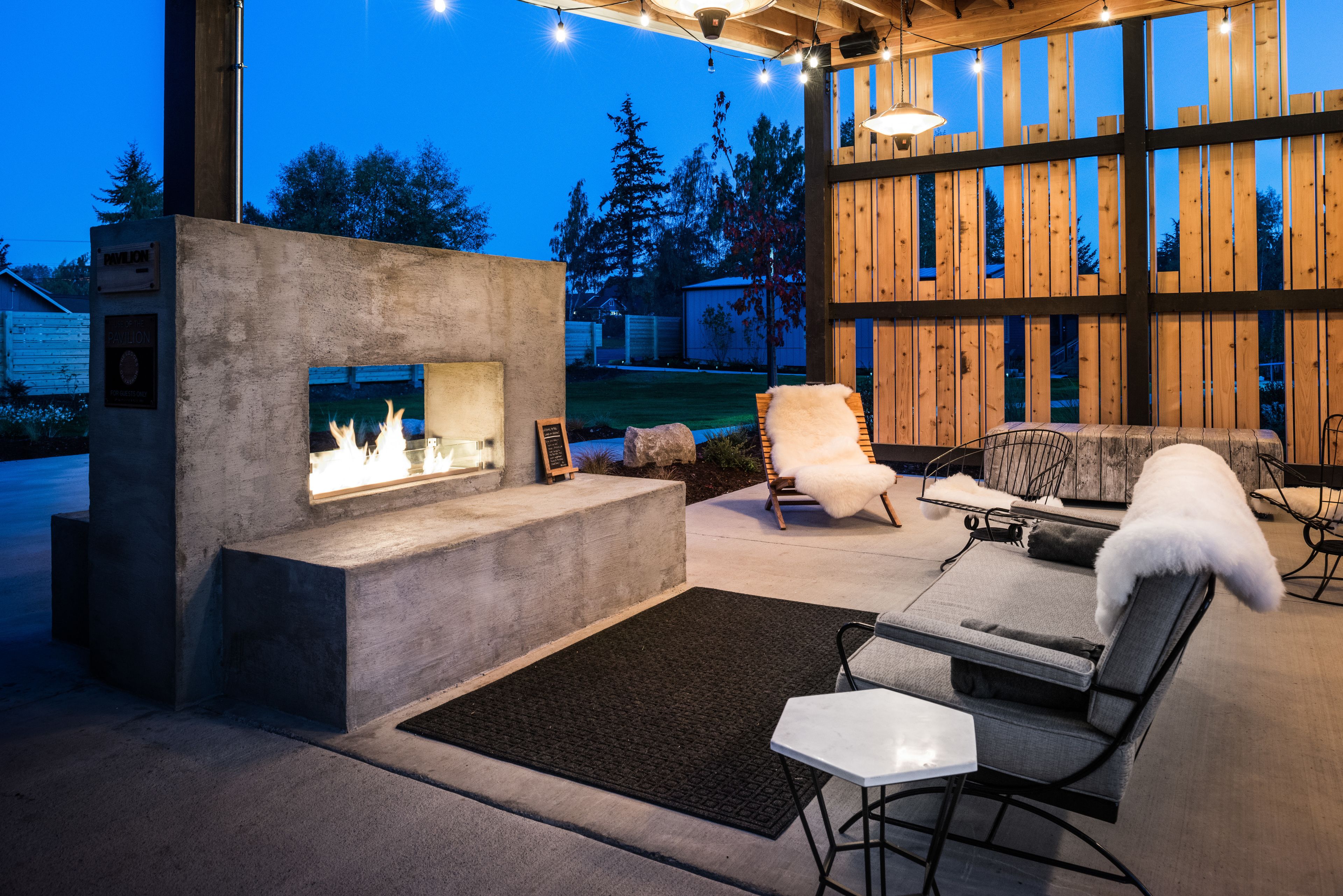 A modern outdoor patio with a concrete fireplace, seating area, and wooden accents.