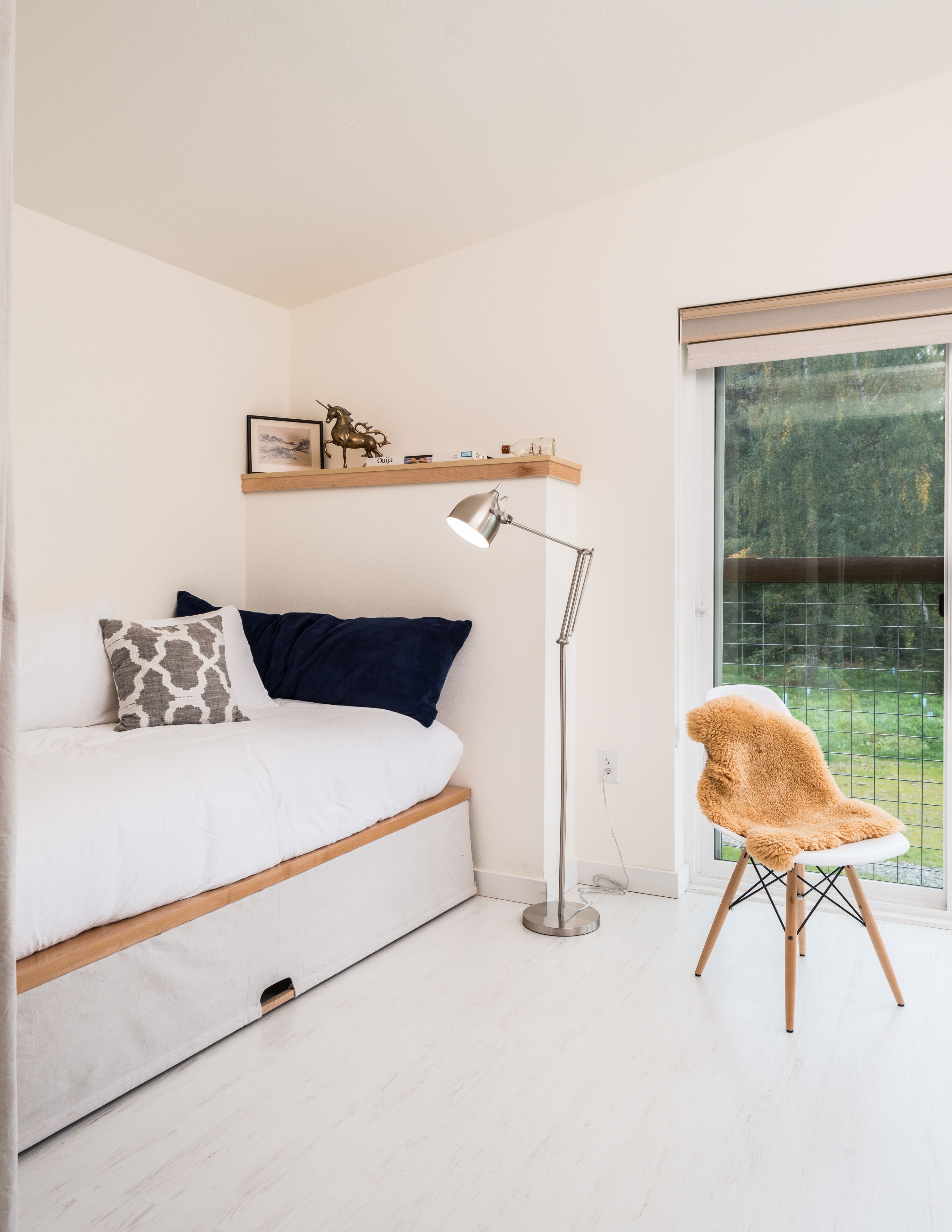 Une chambre à coucher comprenant un lit, une lampe sur pied, une chaise et une fenêtre donnant sur un paysage verdoyant.