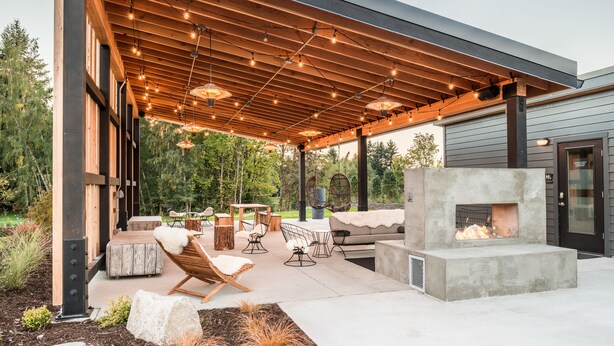 Un patio al aire libre con una pérgola de madera, zona de estar y un hogar a leña integrado.