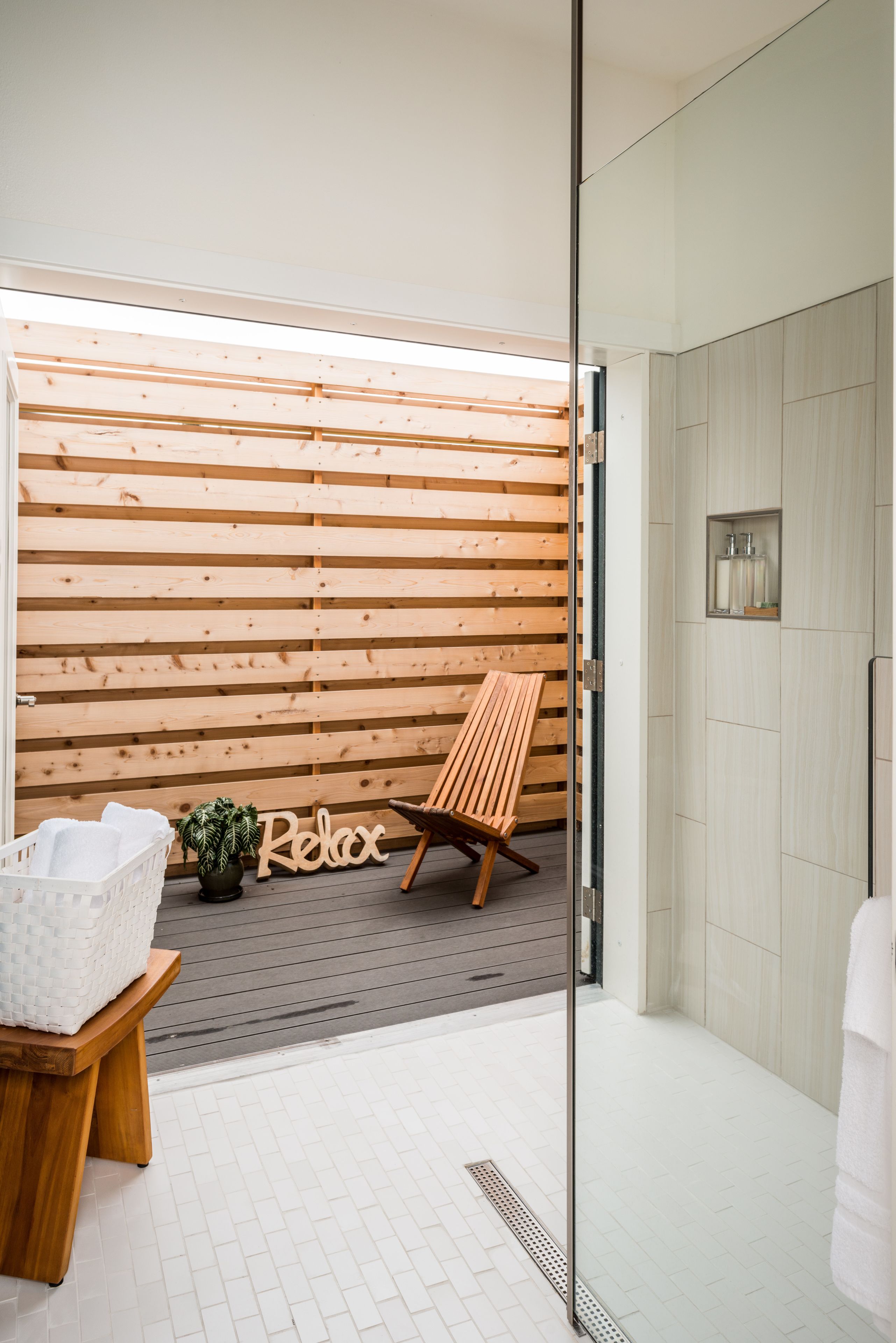A modern bathroom with a wooden slat wall, a bench, a small potted plant, and a 'Relax' sign.