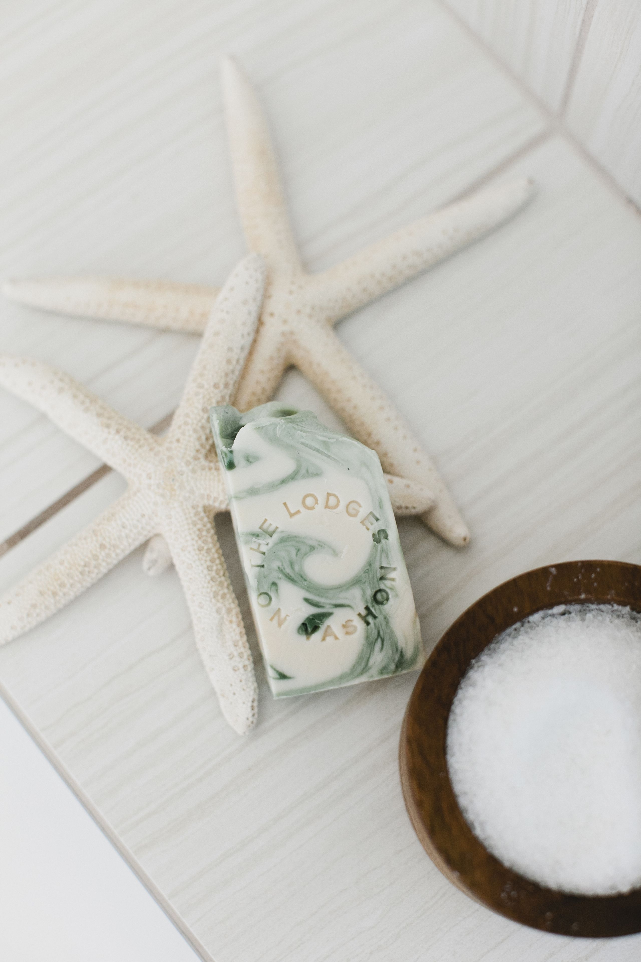 A starfish, a soap bar, and a bowl of salt on a wooden surface.