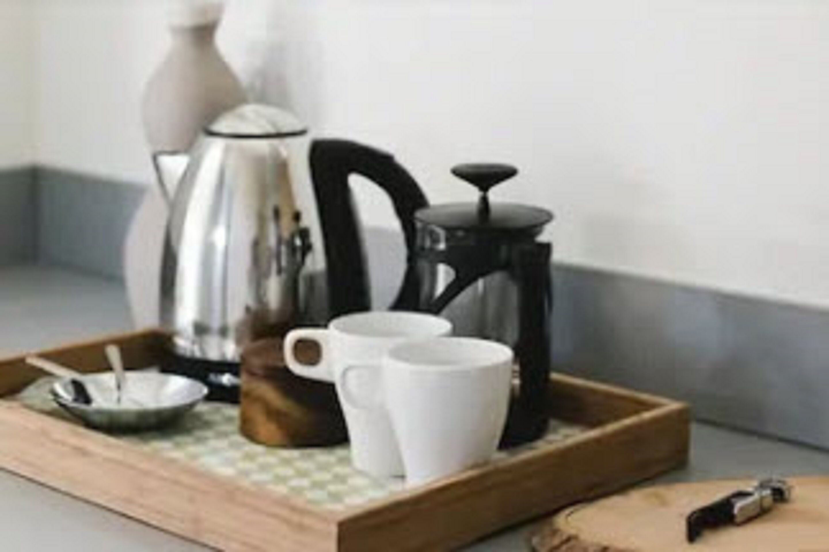 A tray with a coffee maker, two white cups, and a small bowl with a spoon on a wooden surface.