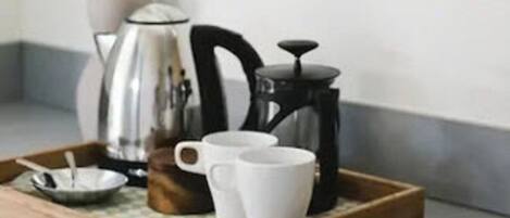 A tray with a coffee maker, two white cups, and a small bowl with a spoon on a wooden surface.