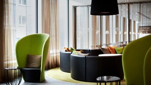 Un hall d’hôtel moderne avec un fauteuil vert, des canapés noirs et une petite table.