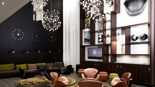 Un salon moderne avec un canapé d’angle, plusieurs fauteuils, un téléviseur et un éclairage décoratif.