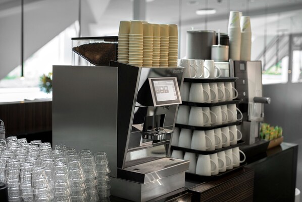 Un espace dédié au café, équipé d’une machine à café, de piles de gobelets jetables et d’une sélection de verres.
