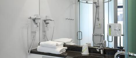 Een moderne badkamer met een rond wastafel, een haardroger, een handdoekrek en een douchehoek.