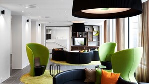Un salon moderne avec un canapé incurvé, un luminaire noir suspendu et un téléviseur en arrière-plan.