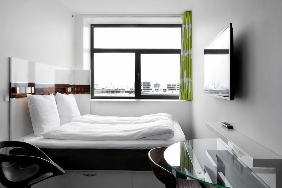 Una habitación de hotel moderna con cama, escritorio, silla, televisión y ventana con vista a la ciudad.