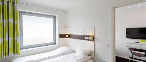 A hotel room with a bed, a TV, a desk, and a window with curtains.