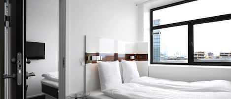 A modern hotel room with a large bed, a bedside table, a flat-screen TV, and a window offering a city view.