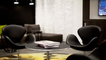 Una habitación moderna con una mesa redonda, dos sillas negras, un sofá y un televisor en la pared.