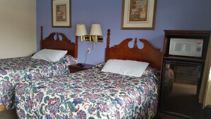 Ein Hotelzimmer mit zwei Betten, einem Nachttisch, einer Lampe, einer Mikrowelle und gerahmten Bildern an der Wand.
