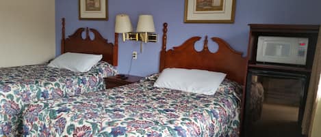 A hotel room with two beds, a nightstand, a lamp, a microwave, and framed pictures on the wall.